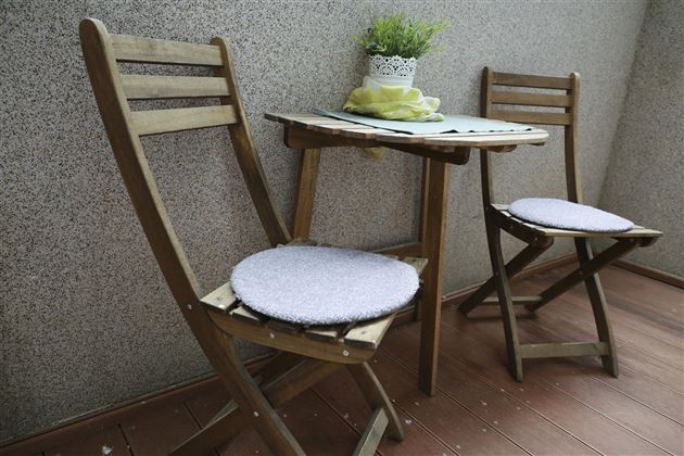 A small balcony with a wooden table and two folding chairs. A small plant is on the table.