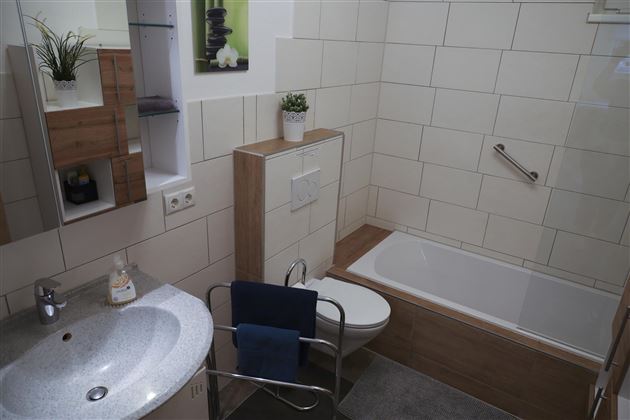 A modern bathroom with a bathtub, a sink, and wood paneling. The walls are light tiled and there are decorative plants.