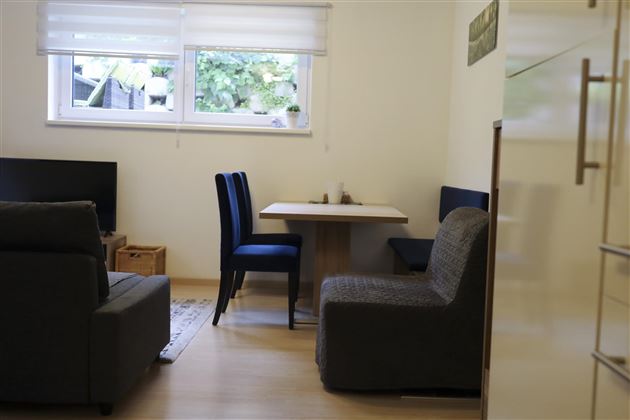 A cozy room with a sofa and a dining area. A table with chairs is placed in front of a window that lets in a lot of light.