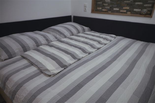 A cozy bed with striped bed sheets and pillows. The colors are in shades of gray and white.