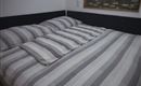 A cozy bed with striped bed sheets and pillows. The colors are in shades of gray and white.