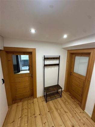 Un corridoio luminoso con porte rivestite in legno e una semplice libreria. Il pavimento è in legno chiaro e le pareti sono bianche.
