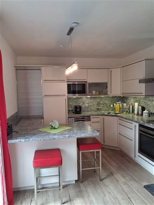 Een moderne keuken met lichte kasten en een granieten werkblad. Rode barkrukken en talrijke keukenapparaten maken het geheel af.