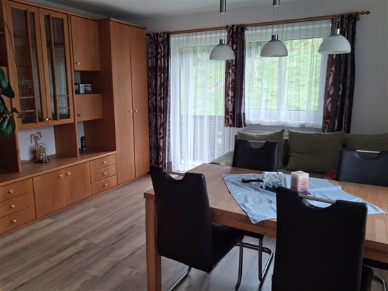 Een gezellige woonkamer met een eethoek en een groot raam. De ruimte is ingericht met een houten tafel, zwarte stoelen en een lichte decoratie.