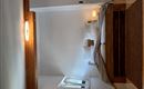 Ein modernes Schlafzimmer mit einem Doppelbett und weißen Kissen. Es gibt holzfarbene Akzente und eine große Fensterfläche, die Tageslicht hereinlässt.