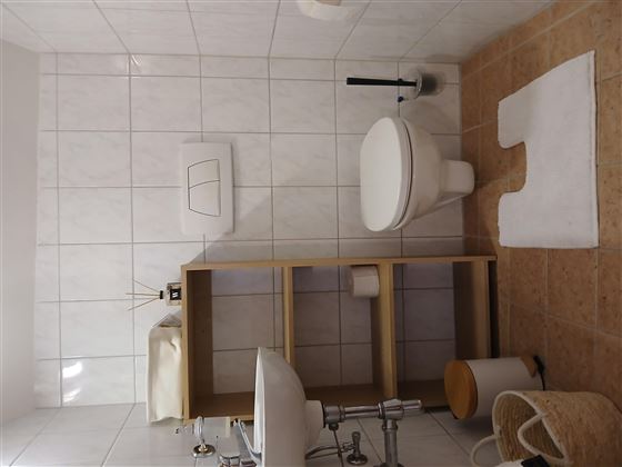 Ein schlichtes Badezimmer mit weißen Fliesen und einem modernen Toilette. Die Ausstattung umfasst eine Handtuchablage und einen kleinen Abfallbehälter.