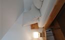 Ein einfaches Schlafzimmer mit einem Bett und zwei Kopfkissen. Neben dem Bett steht ein Nachttisch mit einer Lampe.