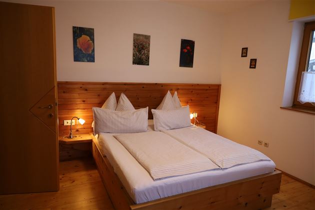 Ein gemütliches Schlafzimmer mit einem Doppelbett und Holzverkleidung. Weiße Wände und dezente Dekoration sorgen für eine einladende Atmosphäre.