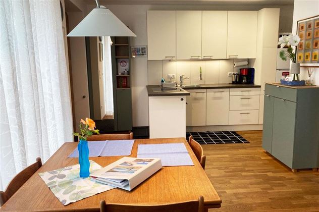 Een moderne keuken met een houten tafel en stoelen. Op de tafel staat een vaas met een bloem en enkele placemats.