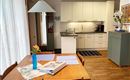 Een moderne keuken met een houten tafel en stoelen. Op de tafel staat een vaas met een bloem en enkele placemats.