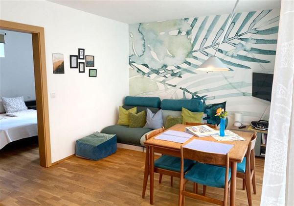 Een moderne woonkamer met een gezellige bank en een eettafel. Aan de muur hangt een kleurrijke, botanische muurschildering.