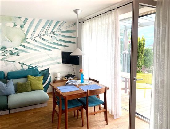 Een heldere en moderne woonkamer met een gezellige bank en een eettafel. Grote ramen laten veel licht binnen en bieden uitzicht op de buitenruimte.