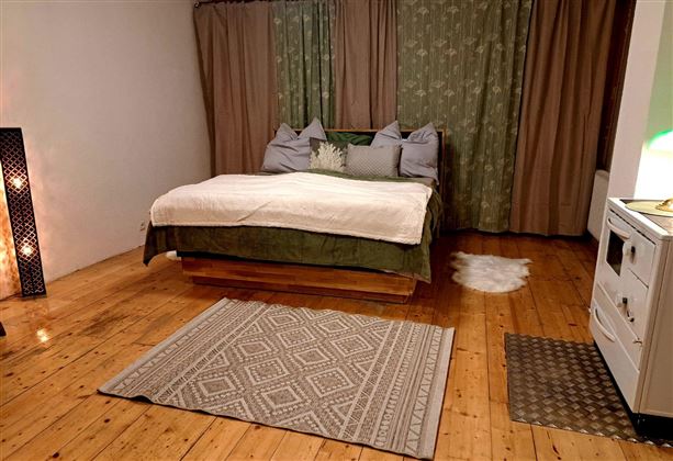A cozy bedroom with a large bed and soft pillows. The wooden floor and warm colors create an inviting atmosphere.