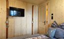 Ein gemütliches Zimmer mit Holzwänden und einem Fernseher an der Wand. Auf dem Bett liegen dekorative Kissen und eine ansprechende Bettdecke.