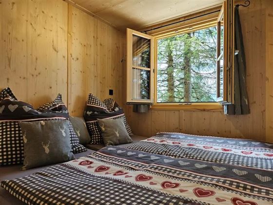 Ein gemütliches Zimmer mit zwei Betten und Kissen. Das Fenster öffnet sich zu einem schönen Blick auf Bäume.