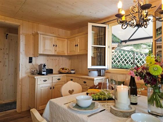Eine gemütliche Küche mit Holzmöbeln und einem gedeckten Tisch. Blumenarrangements und frisches Obst schaffen eine einladende Atmosphäre.