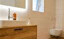Een moderne badkamer met een houten badkamerkast, wastafel en een elegante spiegel. De kamer heeft lichte tegels en een groot raam voor natuurlijk licht.