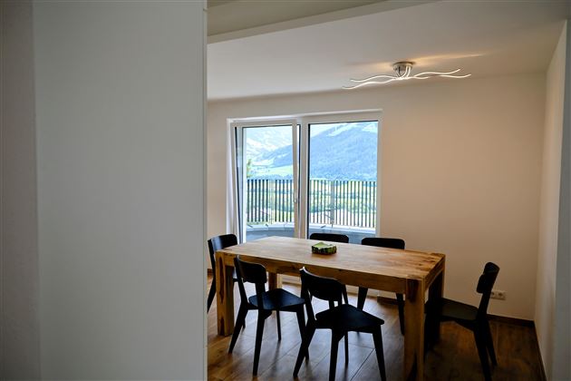 Een lichte eetkamer met een grote houten tafel en zes zwarte stoelen. Vanuit de ramen kijkt men uit op een indrukwekkend berglandschap.