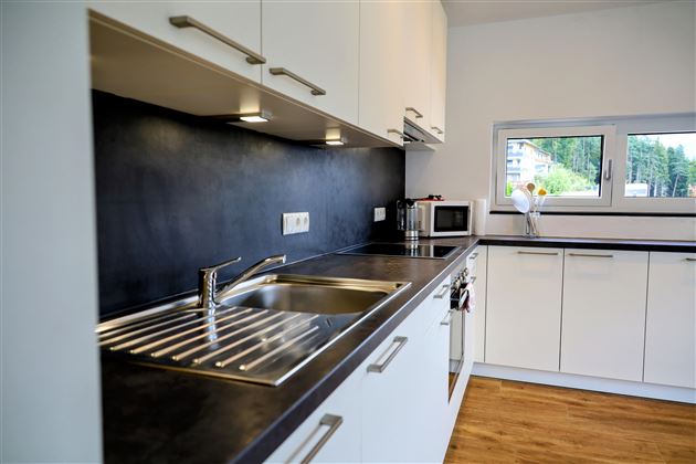 Een moderne keuken met witte kasten en een donker aanrechtblad. Op het aanrecht zijn een spoelbak en een kleine magnetron te zien.