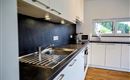 Een moderne keuken met witte kasten en een donker aanrechtblad. Op het aanrecht zijn een spoelbak en een kleine magnetron te zien.