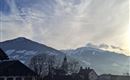 A picturesque mountain landscape with snow-capped peaks and a charming church in the foreground. The sky is clear with gentle clouds.