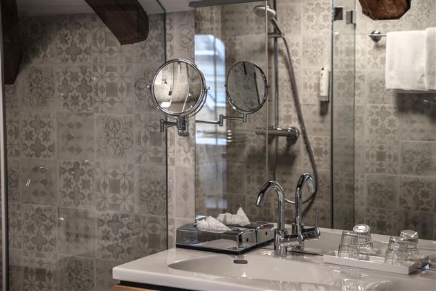 Une salle de bain moderne avec des carreaux élégants et un grand miroir. Les équipements sont en métal chromé et il y a des serviettes fraîches.