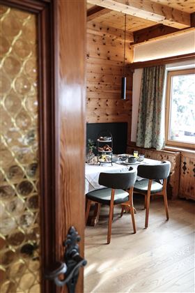Ein gemütlicher Speiseraum mit einem Holztisch und stilvollen Stühlen. Licht strömt durch das Fenster und schafft eine einladende Atmosphäre.