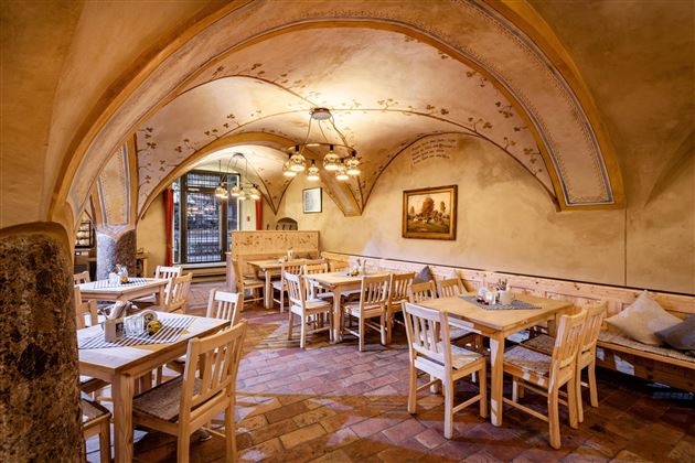 A cozy restaurant with wooden chairs and tables. The ceiling is vaulted and decorated, creating a warm atmosphere.