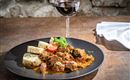 A delicious dish with tender meat in a savory sauce, served with side dishes. Accompanied by a glass of red wine on a rustic table.