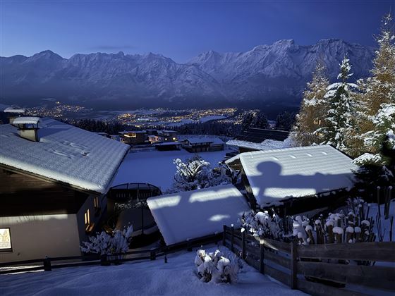 Un paysage enneigé la nuit, entouré de majestueuses montagnes. Les lumières d'une ville scintillent en arrière-plan.