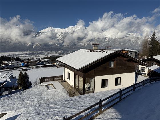 Une maison confortable dans un paysage enneigé. Les montagnes imposantes et le ciel bleu créent une atmosphère hivernale idyllique.