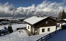 Une maison confortable dans un paysage enneigé. Les montagnes imposantes et le ciel bleu créent une atmosphère hivernale idyllique.