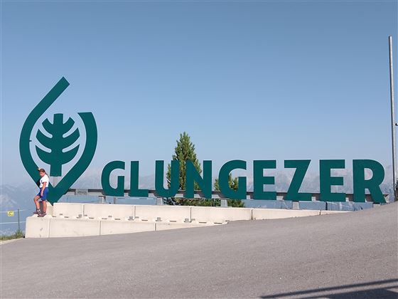 A large green inscription with the word "GLUNGEZER" stands on a mountain. In the background, mountain landscapes are visible.