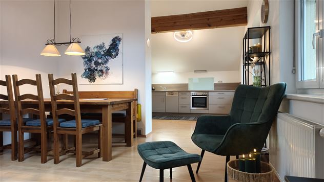 An inviting dining area with a wooden table and chairs. A modern kitchen can be seen in the background.