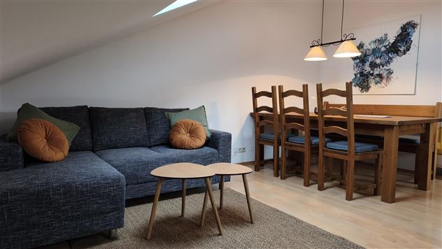 A cozy living room with a blue sofa and a coffee table. In the background, there is a dining area with wooden chairs and a table.
