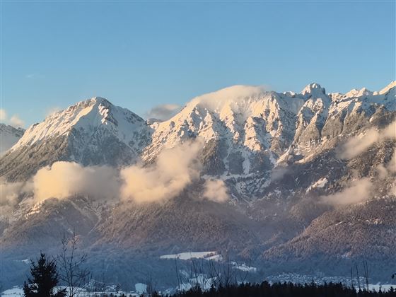 A majestic mountain panorama with snow-covered peaks and gentle clouds. The sky is clear and blue, highlighting the beauty of the landscape.