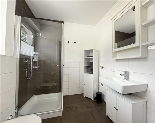 Une salle de bains moderne avec une douche, un lavabo et un miroir. Les murs sont clairs et l'équipement est simple et fonctionnel.