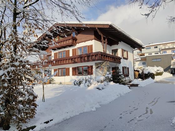 A charming chalet-style house, surrounded by snow-covered trees. The sky is clear and the landscape exudes tranquility.