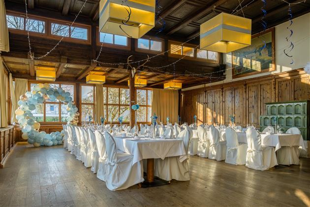 An elegant event space with covered tables and white chairs. There is a decorative balloon installation on the wall.