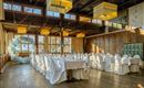 An elegant event space with covered tables and white chairs. There is a decorative balloon installation on the wall.