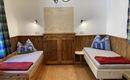 A cozy room with two beds, wooden paneling, and blue cushions. 

Checkered curtains hang on the walls, and there is a wooden wardrobe in the middle.