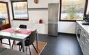 Eine moderne Küche mit einem Esstisch und Stühlen. An der Wand sind Fenster, die viel Licht hereinlassen.