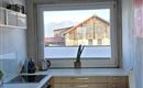 Eine moderne Küche mit Holzschränken und einem großen Fenster. Draußen sind Dächer von Gebäuden sichtbar.