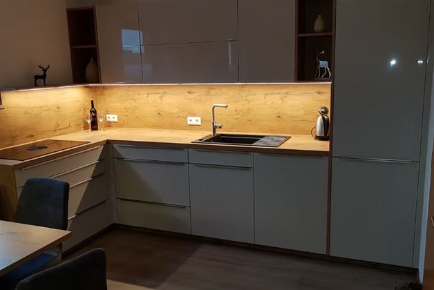 A modern kitchen with bright wood surfaces and understated furniture. The lighting creates a pleasant atmosphere.