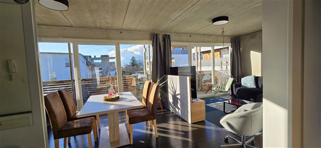 Ein helles und modernes Wohnzimmer mit einem Essbereich. Große Fenster bieten viel Tageslicht und einen Blick nach draußen.