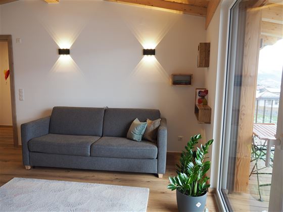 Un soggiorno moderno con un divano grigio e una pianta. Le pareti sono chiare e c'è un'illuminazione soffusa.