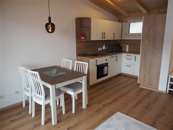 Una cucina moderna con un tavolo da pranzo e sedie bianche. La stanza ha dettagli in legno chiaro e molta luce naturale.