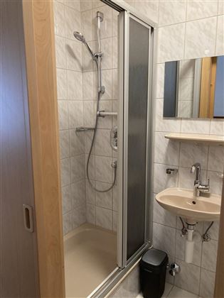 A modern bathroom with a shower cubicle and a sink. The walls are tiled and there is a small mirror above the sink.