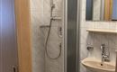 A modern bathroom with a shower cubicle and a sink. The walls are tiled and there is a small mirror above the sink.
