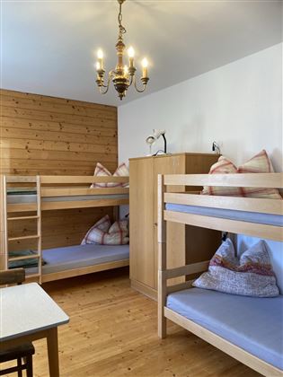 A cozy room with bunk beds and wooden paneling. A bright lamp hangs from the ceiling and there are several pillows on the beds.